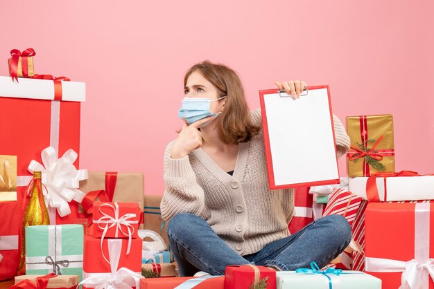 Vooraanzicht jonge vrouw zitten rond kerstcadeautjes in masker met notitie