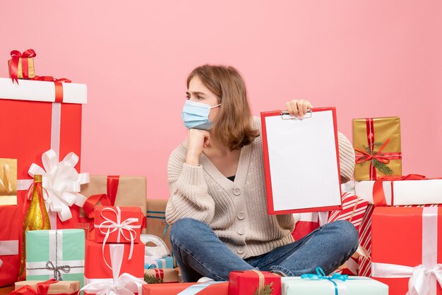 Vooraanzicht jonge vrouw zitten rond kerstcadeautjes in masker met notitie