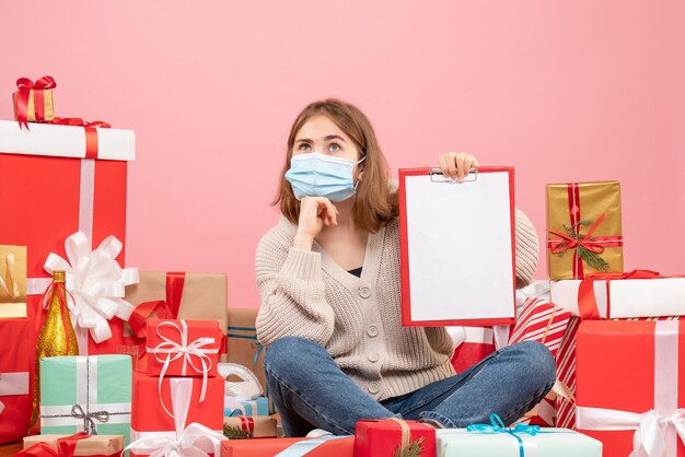 Vooraanzicht jonge vrouw zitten rond kerstcadeautjes in masker met notitie