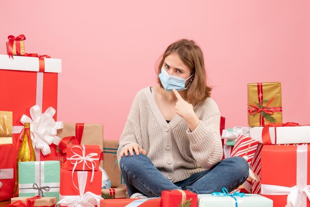 Gratis foto vooraanzicht jonge vrouw zitten rond kerstcadeautjes in steriel masker