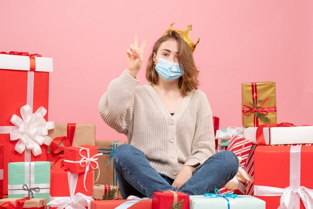 Vooraanzicht jonge vrouw zitten rond kerstcadeautjes in steriel masker