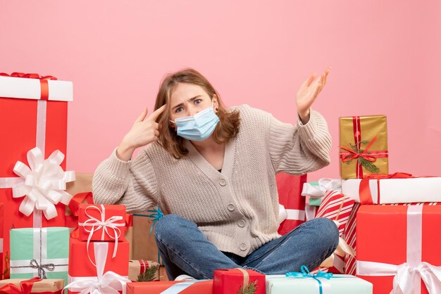 Vooraanzicht jonge vrouw zitten rond kerstcadeautjes in steriel masker