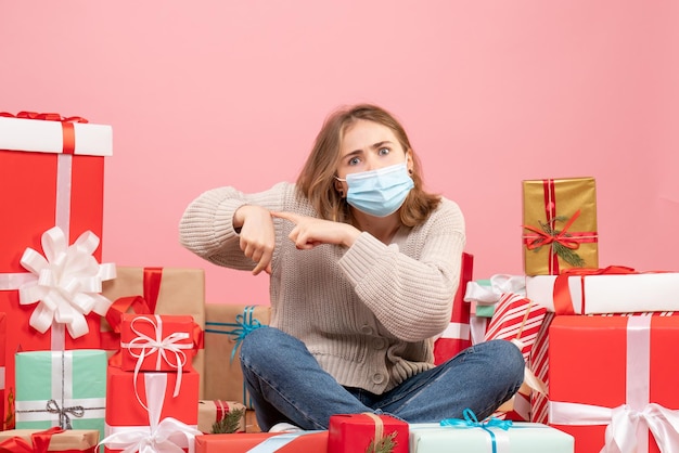 Vooraanzicht jonge vrouw zitten rond kerstcadeautjes in steriel masker