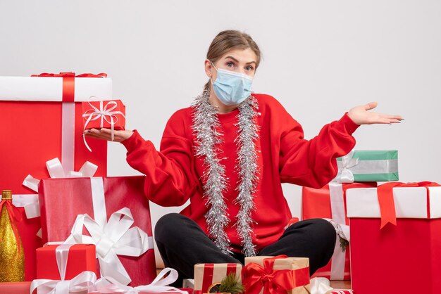 Vooraanzicht jonge vrouw zittend rond kerstcadeautjes in steriel masker