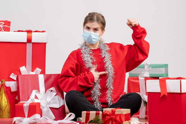 Vooraanzicht jonge vrouw zittend rond kerstcadeautjes in steriel masker