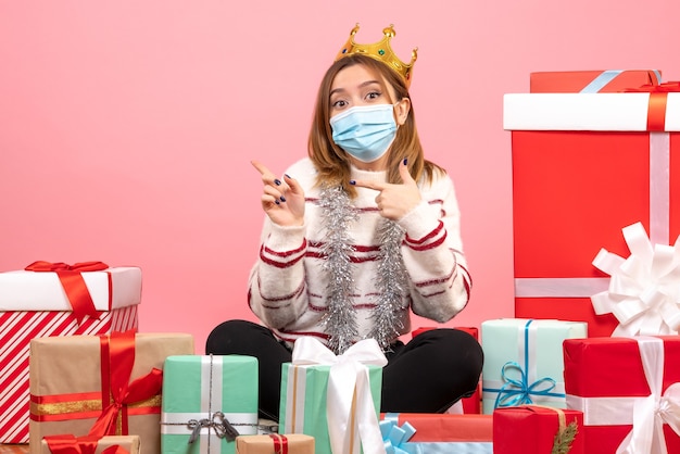 Vooraanzicht jonge vrouw zittend rond kerstcadeautjes in steriel masker