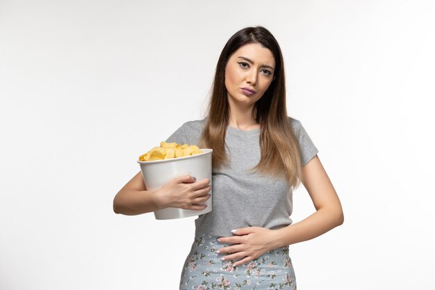 Vooraanzicht jonge vrouwelijke aardappelchips te houden tijdens het kijken naar film op wit oppervlak