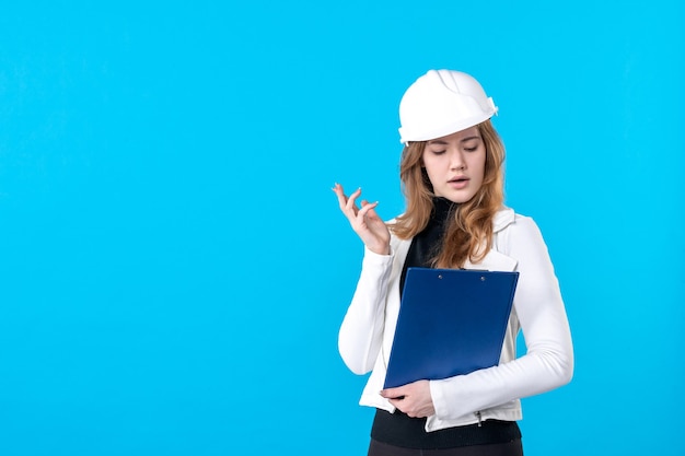 Vooraanzicht jonge vrouwelijke architect in helm op blauw