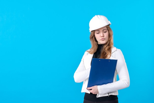 Vooraanzicht jonge vrouwelijke architect in helm op blauw