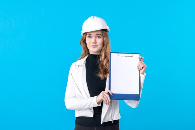 Vooraanzicht jonge vrouwelijke architect in helm op blauw