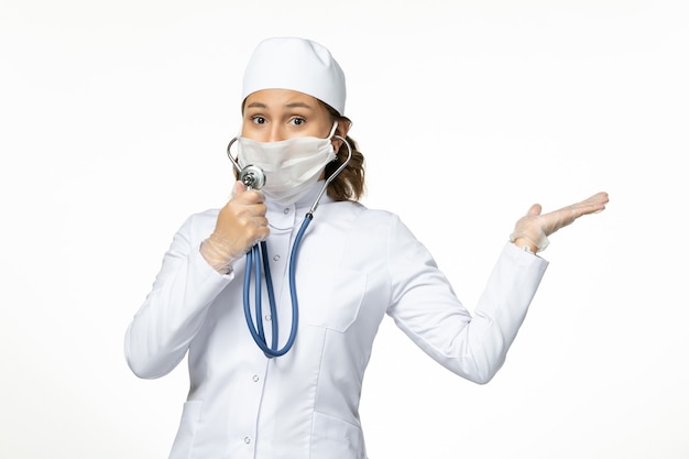 Vooraanzicht jonge vrouwelijke arts die een beschermend steriel masker draagt vanwege het coronavirus met een stethoscoop op een wit bureau