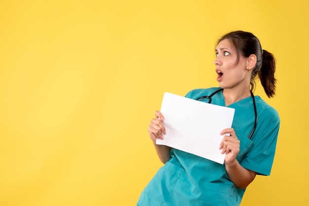 Vooraanzicht jonge vrouwelijke arts in medisch overhemd die document analyse op gele achtergrond houden