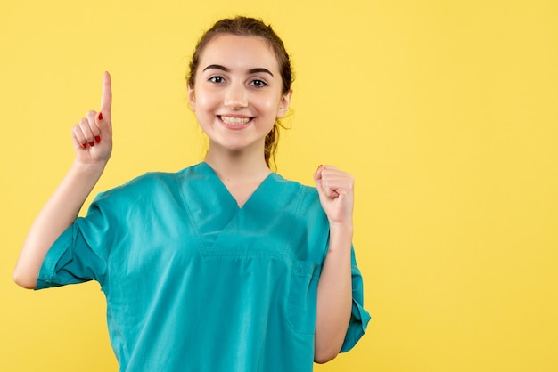 Vooraanzicht jonge vrouwelijke arts in medisch pak op gele achtergrond