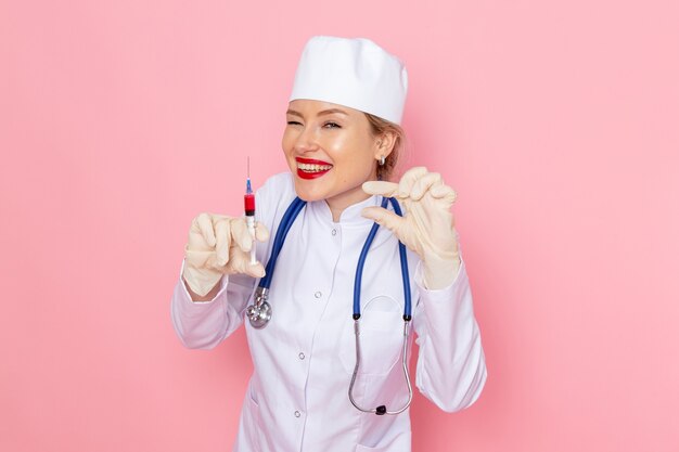 Vooraanzicht jonge vrouwelijke arts in wit medisch pak met blauwe stethoscoop injectie op de roze ruimte geneeskunde medische ziekenhuis werknemer vrouwelijke baan te houden