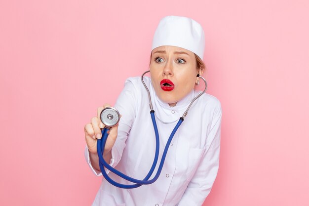 Vooraanzicht jonge vrouwelijke arts in wit pak met blauwe stethoscoop poseren en meten op de roze ruimte vrouwelijke werk
