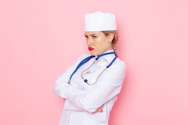 Vooraanzicht jonge vrouwelijke arts in wit pak met blauwe stethoscoop poseren met ontevreden uitdrukking op de roze ruimte baan geneeskunde medische ziekenhuis arts