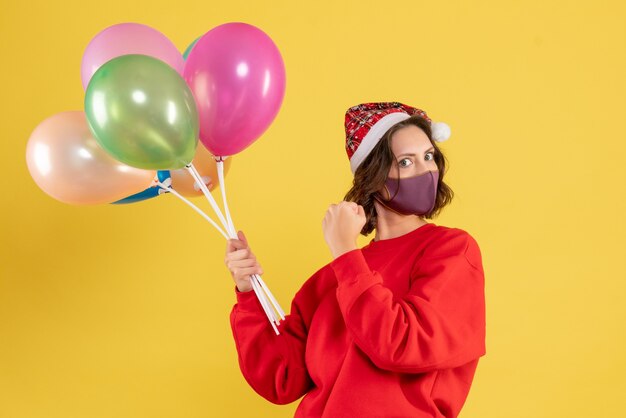 Vooraanzicht jonge vrouwelijke bedrijf ballonnen in steriel masker op geel