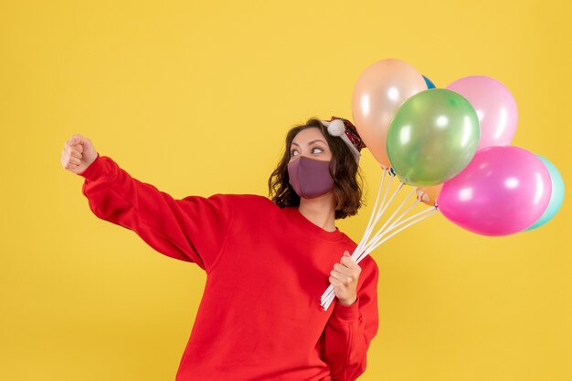 Vooraanzicht jonge vrouwelijke bedrijf ballonnen in steriel masker op geel