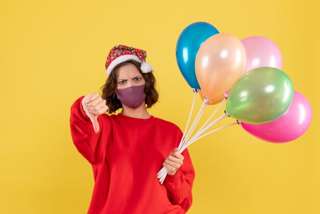 Vooraanzicht jonge vrouwelijke bedrijf ballonnen in steriel masker op geel