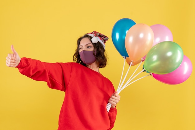 Vooraanzicht jonge vrouwelijke bedrijf ballonnen in steriel masker op geel