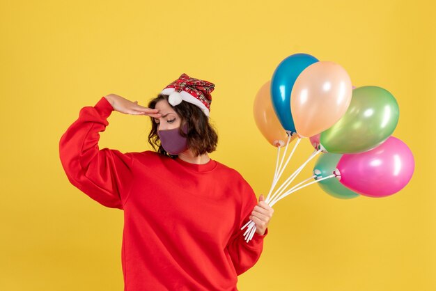 Vooraanzicht jonge vrouwelijke bedrijf ballonnen in steriel masker op geel