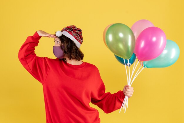 Vooraanzicht jonge vrouwelijke bedrijf ballonnen in steriel masker op geel