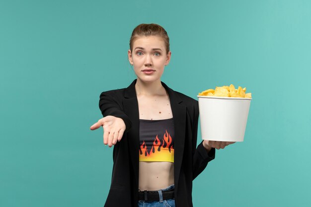 Vooraanzicht jonge vrouwelijke bedrijf chips en kijken naar film op het blauwe oppervlak