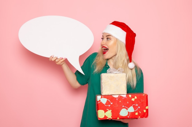 Vooraanzicht jonge vrouwelijke bedrijf kerstcadeautjes en wit bord op roze muur vrouw cadeau sneeuw foto nieuwjaarsvakantie