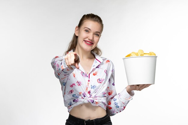 Vooraanzicht jonge vrouwelijke bedrijf mand met chips lachend op wit oppervlak
