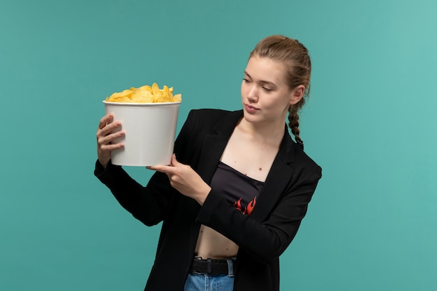 Vooraanzicht jonge vrouwelijke bedrijf pakket met chips en kijken naar film op het lichtblauwe oppervlak