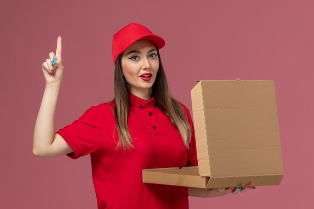 Vooraanzicht jonge vrouwelijke koerier in rode uniforme levering voedseldoos op het roze bureau service levering uniform bedrijf