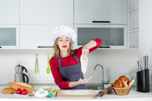 Vooraanzicht jonge vrouwelijke kok in koksmuts en schort met deeg in de keuken