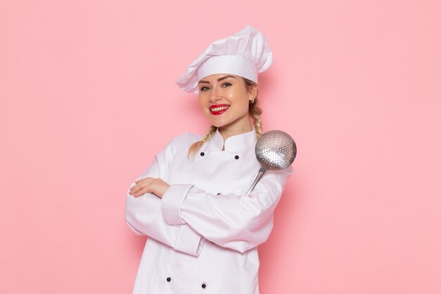 Vooraanzicht jonge vrouwelijke kok in wit kokkostuum poseren met opgetogen uitdrukking op de roze foto van de ruimtekok
