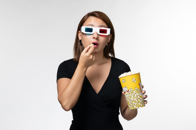 Vooraanzicht jonge vrouwelijke popcorn houden en eten in d zonnebril kijken naar film op wit oppervlak