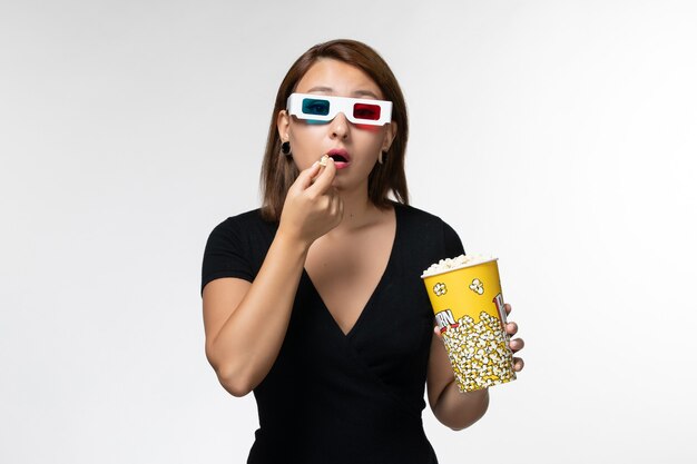 Vooraanzicht jonge vrouwelijke popcorn houden en eten in d zonnebril kijken naar film op wit oppervlak