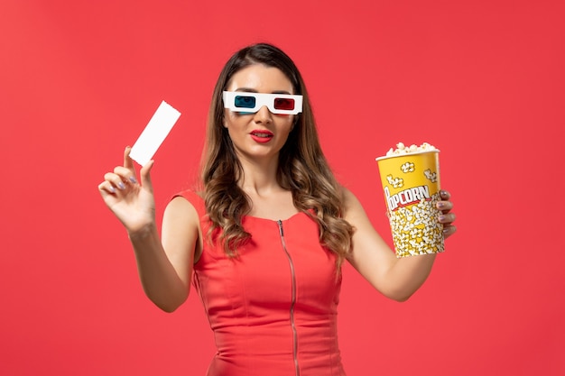 Vooraanzicht jonge vrouwelijke popcorn met kaartje in d zonnebril op rode ondergrond