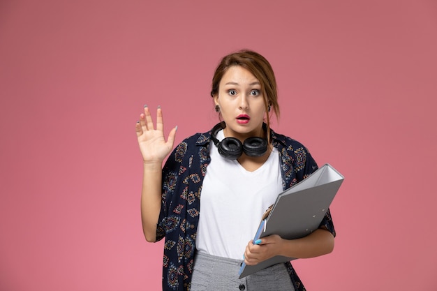 Vooraanzicht jonge vrouwelijke student in wit t-shirt en grijze broek met grijs bestand op de roze achtergrond student lessen hogeschool