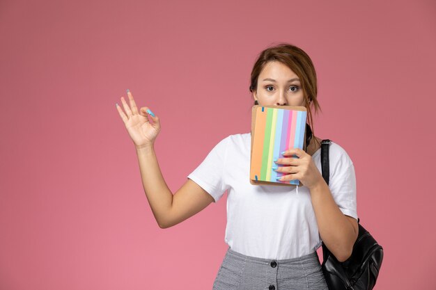 Vooraanzicht jonge vrouwelijke student in witte t-shirt met voorbeeldenboeken met verbaasde uitdrukking op de roze achtergrond les universiteit college studeren boek