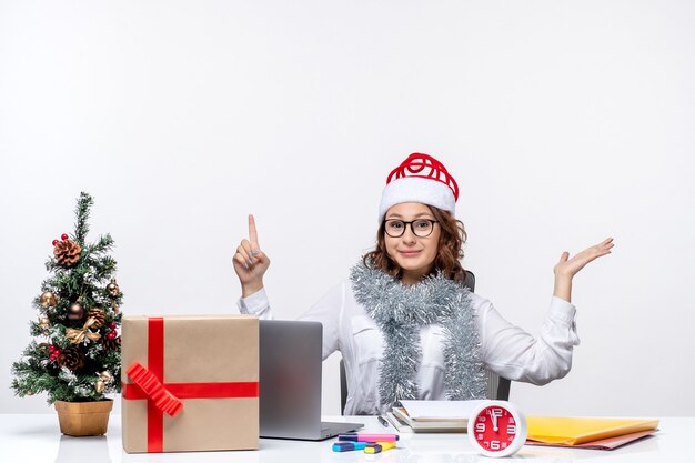 Vooraanzicht jonge vrouwelijke werknemer zittend voor haar werkplek op witte vloer business tafel kantoor baan werk xmas vrouw