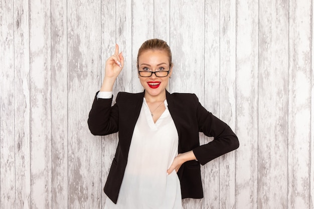 Gratis foto vooraanzicht jonge zakenvrouw in strikte kleding zwarte jas met optische zonnebril lachend op wit bureau werk baan kantoor zakelijke vrouw dame