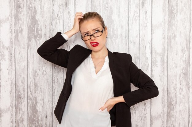 Vooraanzicht jonge zakenvrouw in strikte kleding zwarte jas met optische zonnebril poseren denken op wit bureau werk baan kantoor zakenvrouw dame