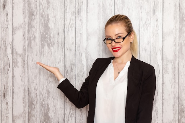 Gratis foto vooraanzicht jonge zakenvrouw in strikte kleding zwarte jas met optische zonnebril poseren en lachend op witte muur werk job kantoor vrouwelijke bedrijf