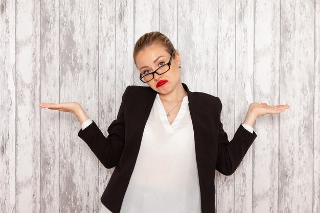 Vooraanzicht jonge zakenvrouw in strikte kleding zwarte jas met optische zonnebril poseren op witte muur job office business woman lady