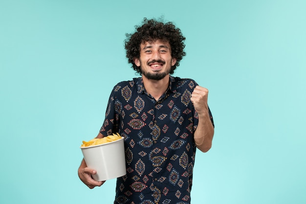 Vooraanzicht jongeman met aardappel cips en vreugde op een blauwe muur mannelijke bioscoop bioscoop filmtheater