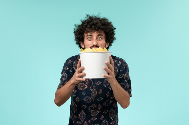 Vooraanzicht jongeman met aardappel cips op de lichtblauwe muur mannelijke bioscoop bioscoop filmtheater