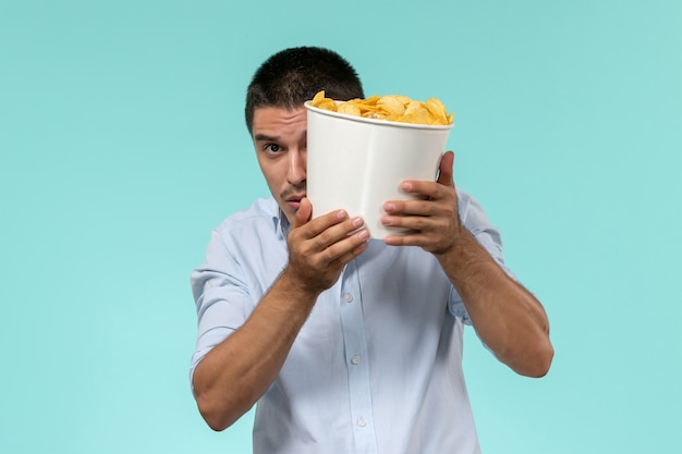 Vooraanzicht jongeman met aardappel cips tijdens het kijken naar film op lichtblauwe muur eenzame afgelegen mannelijke filmbioscoop