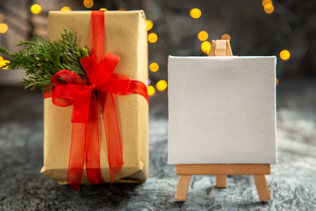 Vooraanzicht kerstcadeau vastgebonden met rood lint wit canvas op houten ezel kerstverlichting op donker