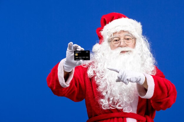 Vooraanzicht kerstman in rood pak met zwarte bankkaart op de blauwe kleur vakantiecadeau xmas