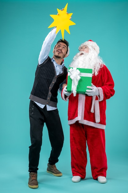 Gratis foto vooraanzicht kerstman met jong mannetje dat geel teken op blauw bureau houdt