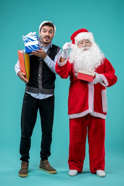 Gratis foto vooraanzicht kerstman met jong mannetje en cadeautjes op blauwe vloer vakantie sneeuw nieuwjaar vakantie xmas